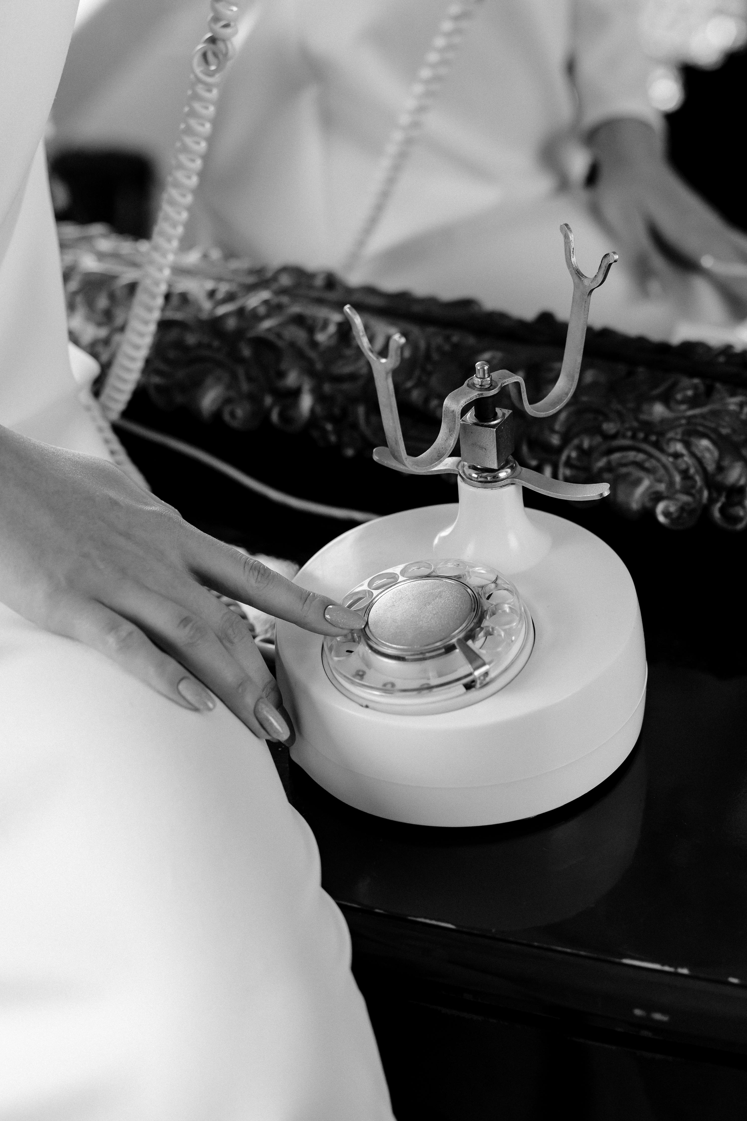 Black and white image of a vintage rotary phone touched by an elegant hand, evoking a classic feel.