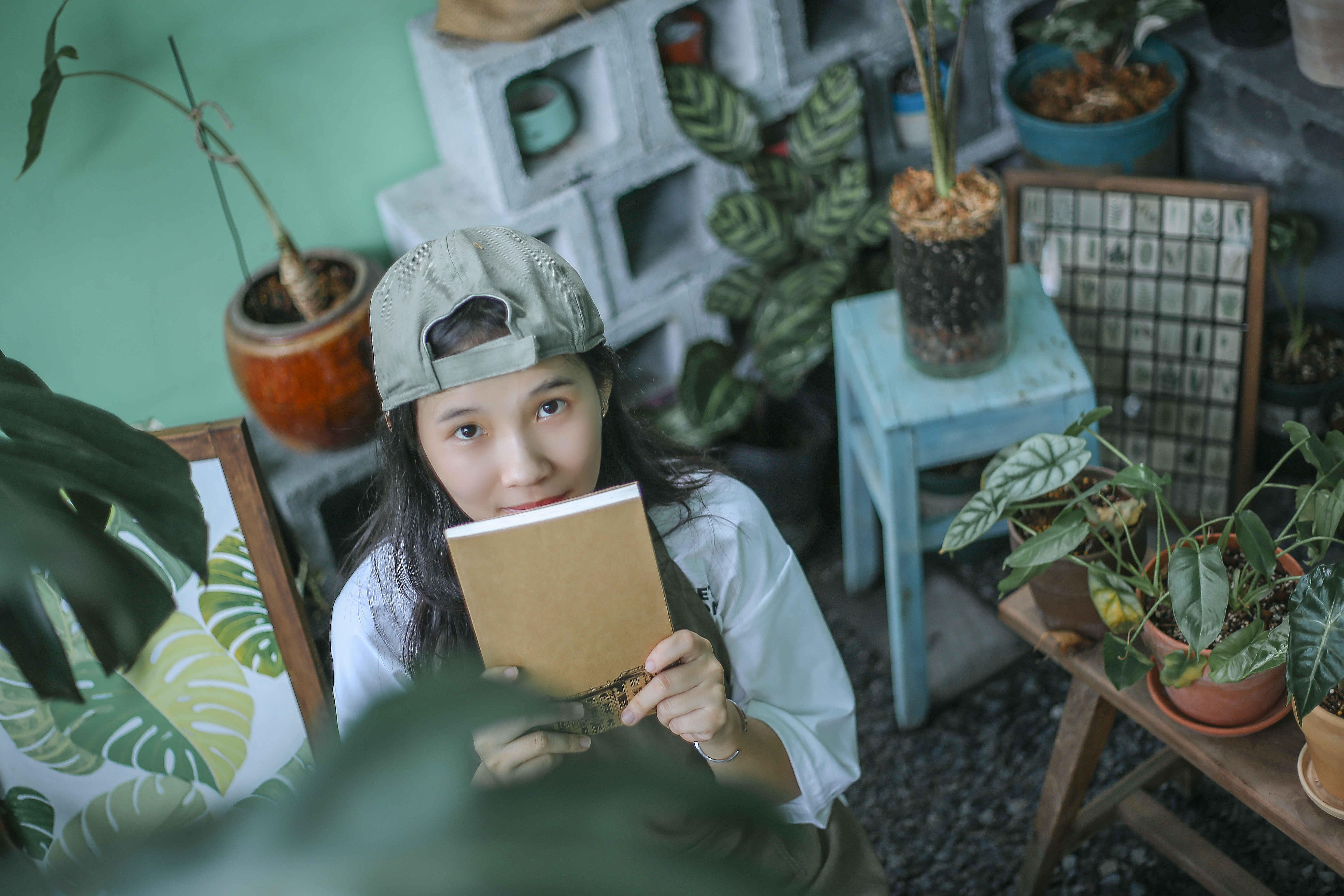 Asian woman holding a notebook surrounded by lush plants in a Hồ Chí Minh garden setting.