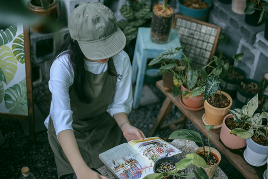 Woman in White Shirt and Green Apron Sitting beside Potted Plants