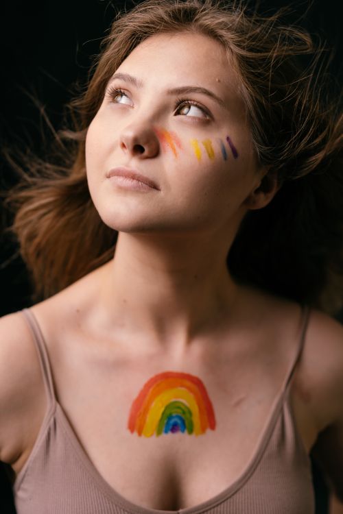 Free A woman with rainbow face paint looks upward, embodying pride and hope. Stock Photo