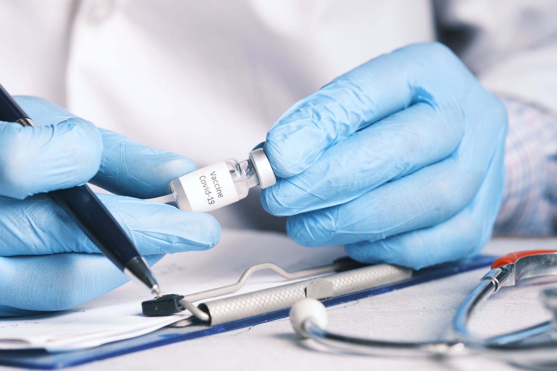 Close-up of a doctor's hands holding a COVID-19 vaccine vial, wearing gloves.