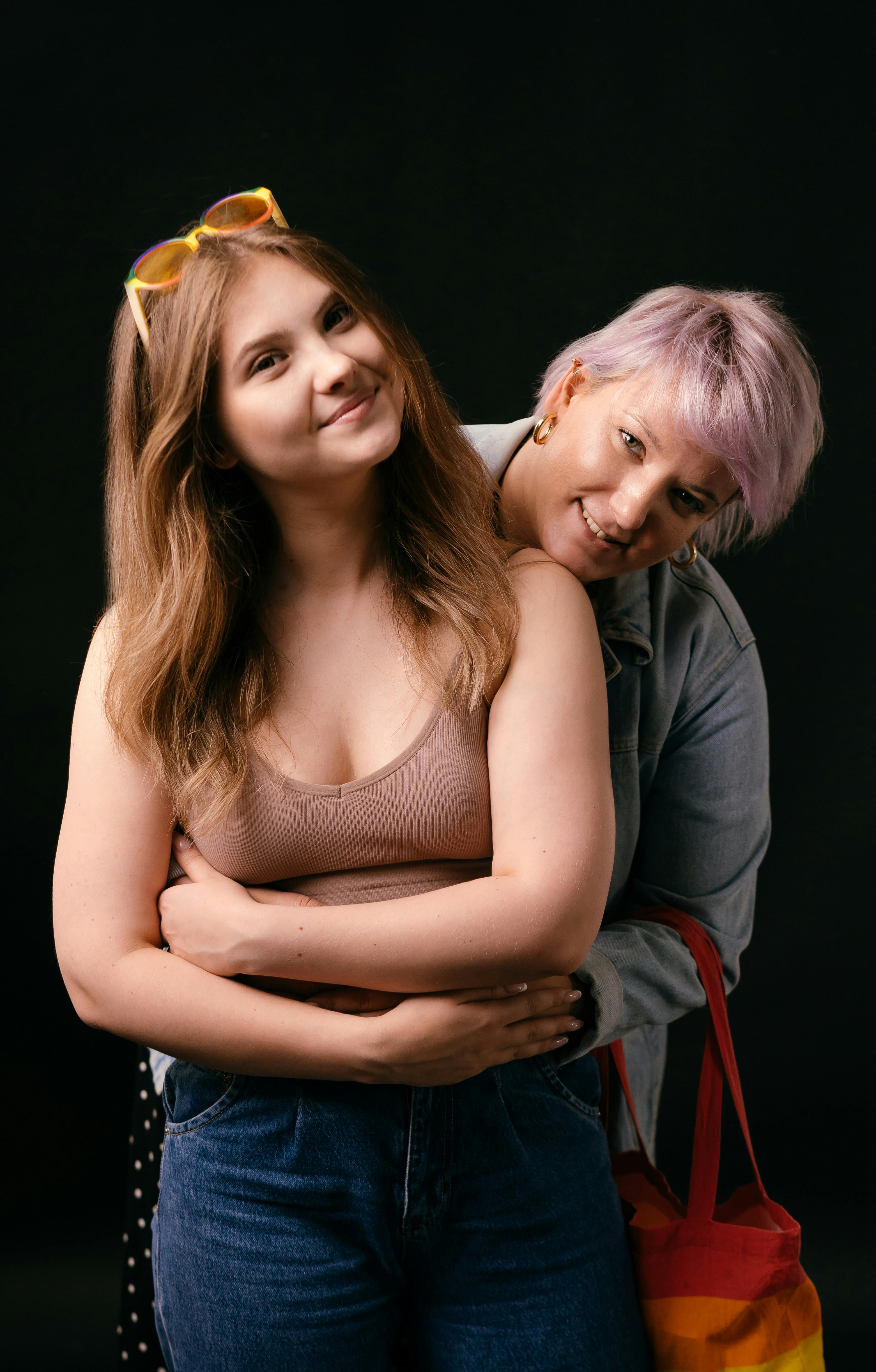 a woman in denim top hugging a woman in brown tank top