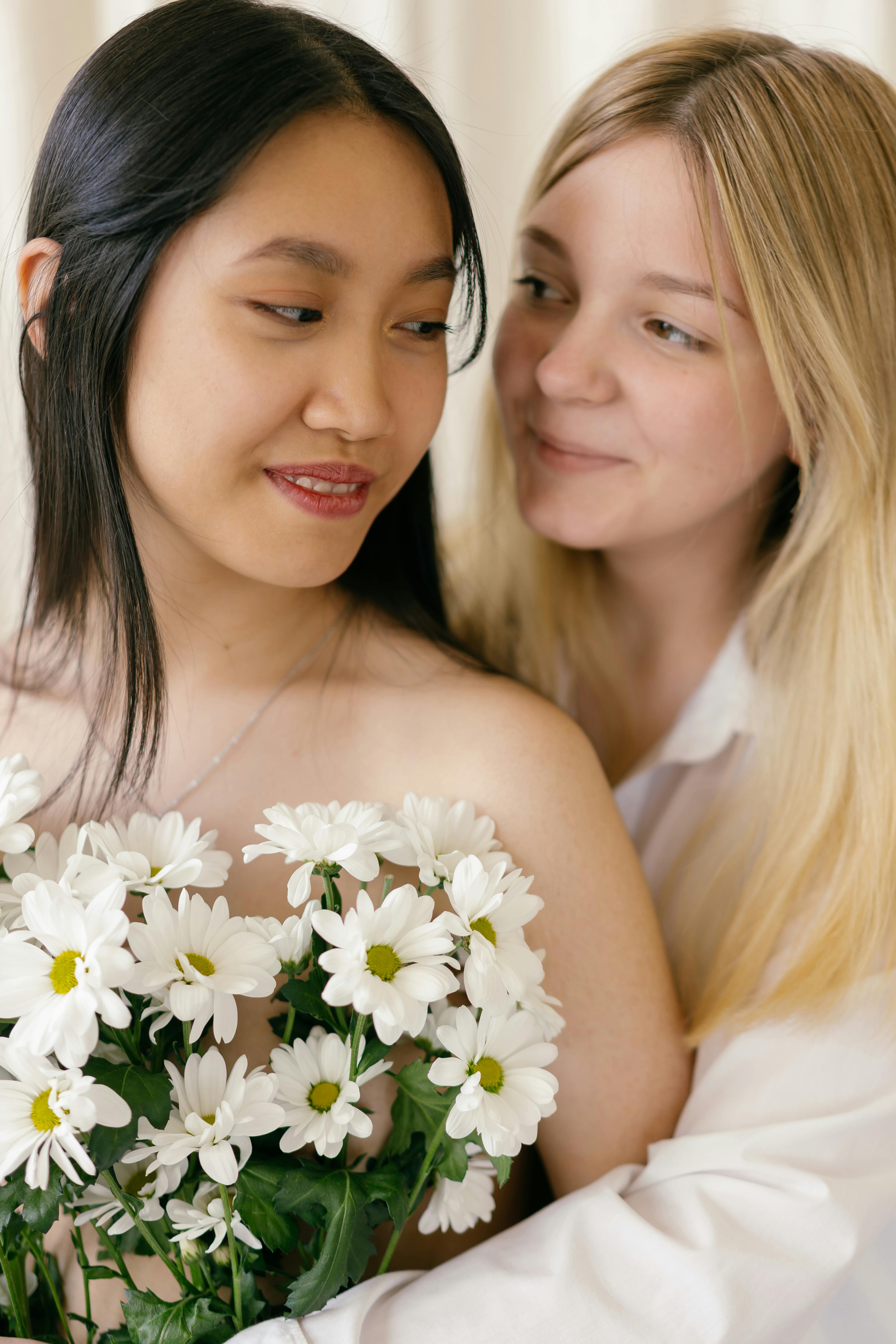 a woman in white long sleeve shirt hugging a woman holding a bouquet of flowers