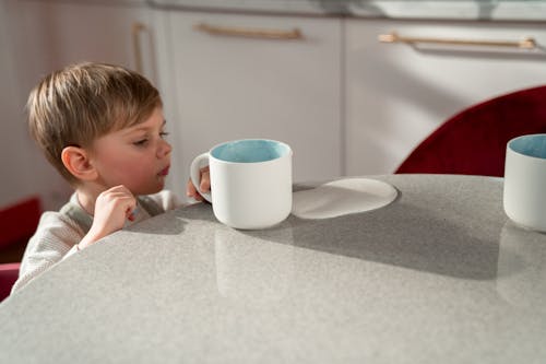 Boy Beside a Table Holding a White Ceramic Mug