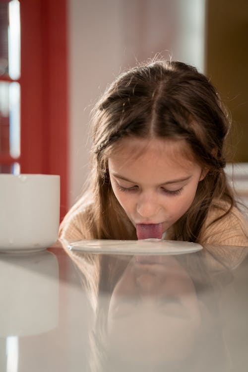 Little Girl Licking Yogurt off Kitchen Table