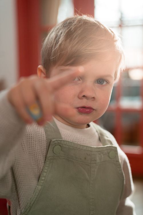 Free Cute young boy with blond hair pointing, lit by sunlight indoors. Stock Photo