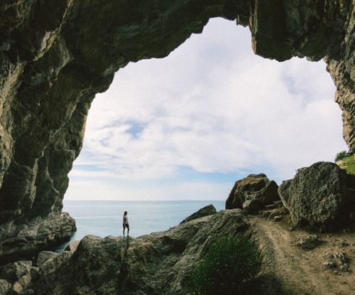 Free Adventurer stands under a massive cave arch, gazing at the ocean. Captures the essence of exploration. Stock Photo