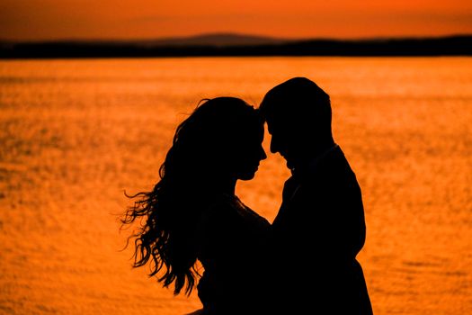A romantic silhouette of a couple embracing at sunset on a serene beach.