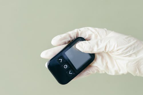 A Person in Latex Gloves Holding a Glucometer Device
