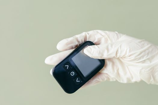 Close-up of a hand in latex gloves holding a blood glucose meter, symbolizing diabetes management.