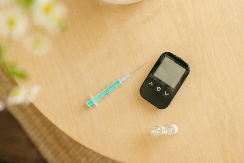 Close-Up Shot of a Black Glucometer beside a Syringe 