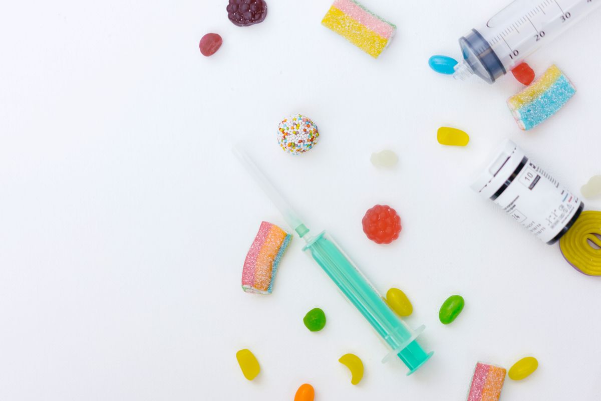 A playful arrangement of colorful candies, syringe, and pill bottle on a white background.