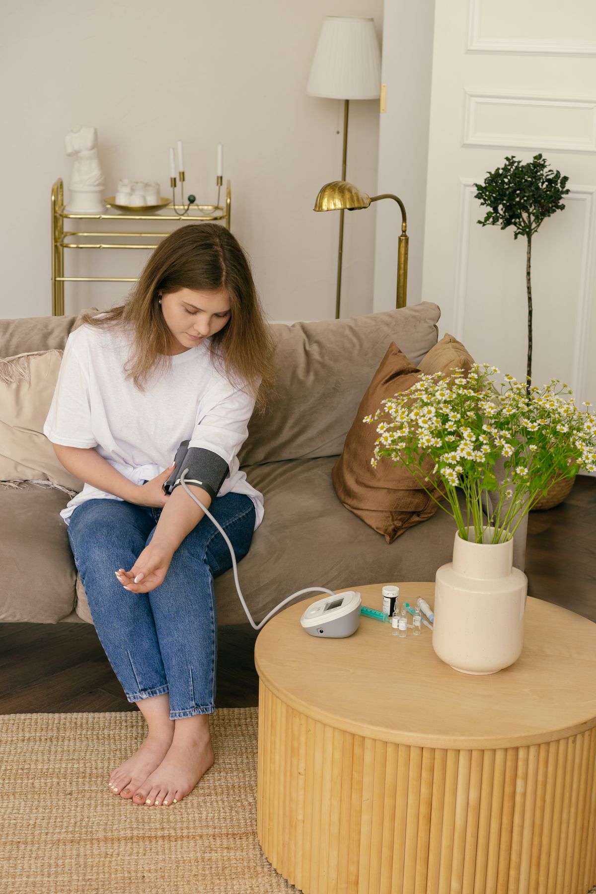 A woman measuring her blood pressure with a home monitor while sitting on a sofa