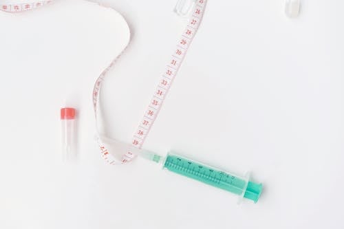 A Syringe and a Tape Measure Lying on White Background 