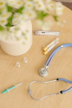 Medical tools with a stethoscope, syringes, and flowers on a table.