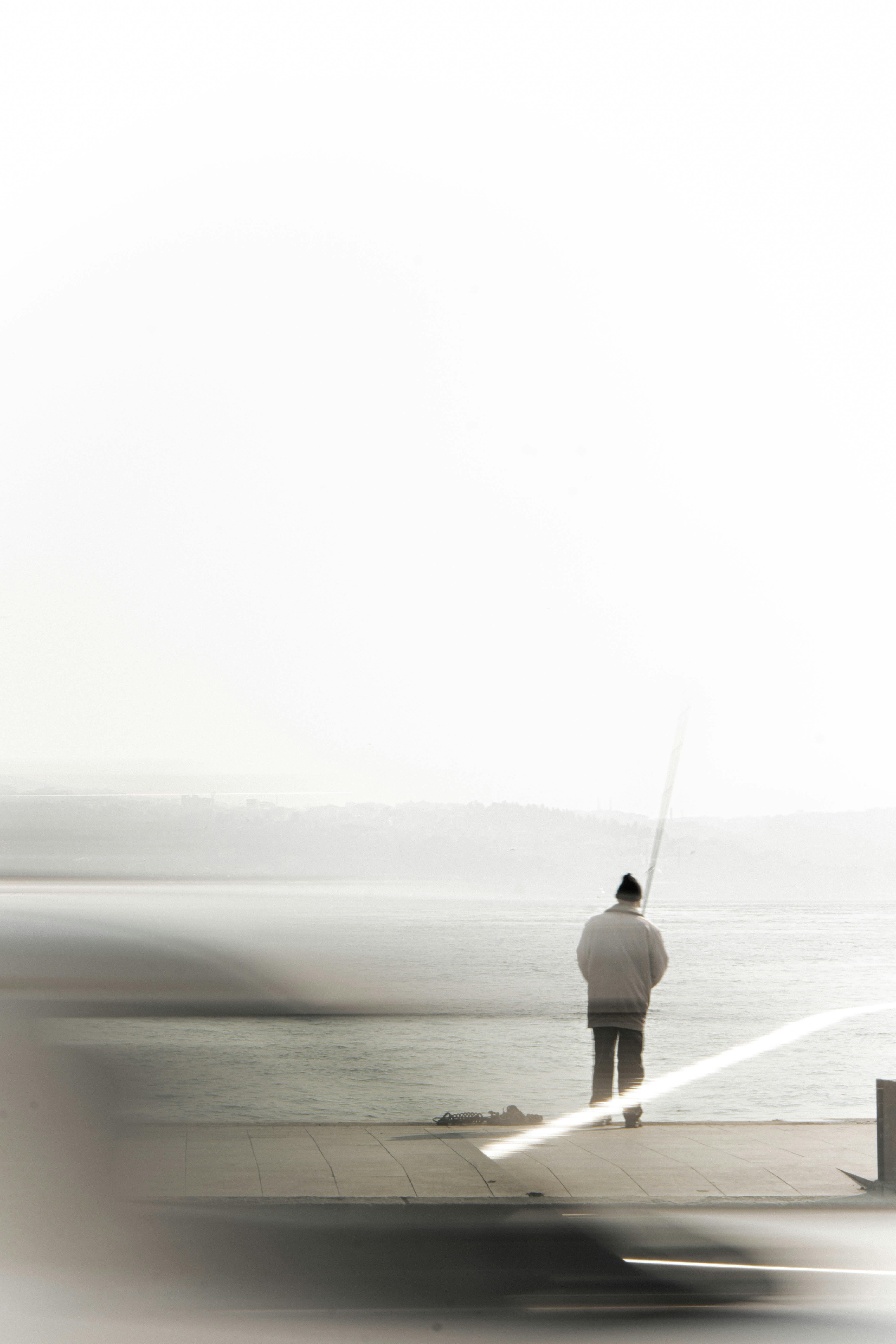 A lone fisherman casts a line on a tranquil lakeside dock, embodying solitude and peace.
