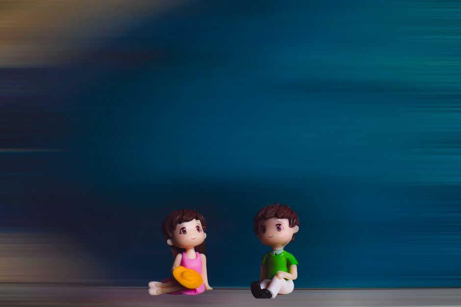 Two cute figurines sitting with a colorful blurred background.