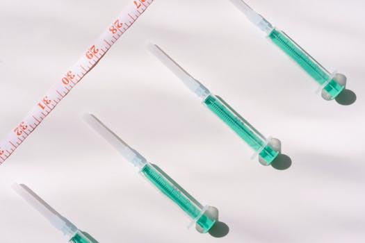 Top view of green filled syringes and measuring tape on a white background, emphasizing healthcare themes.