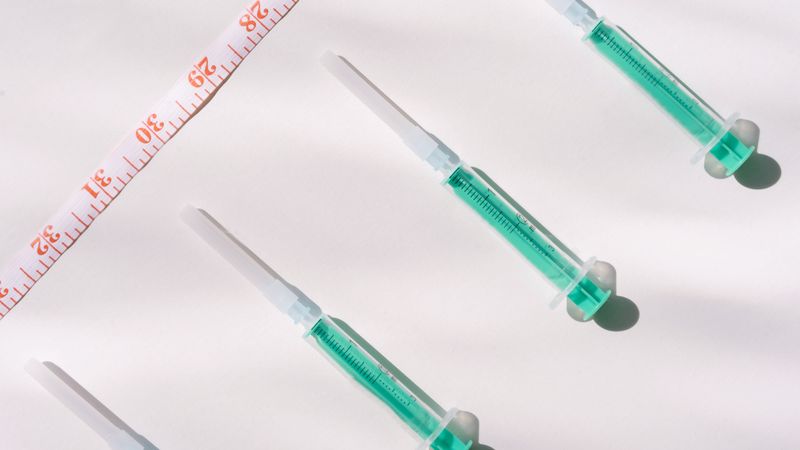 Top view of green filled syringes and measuring tape on a white background, emphasizing healthcare themes.