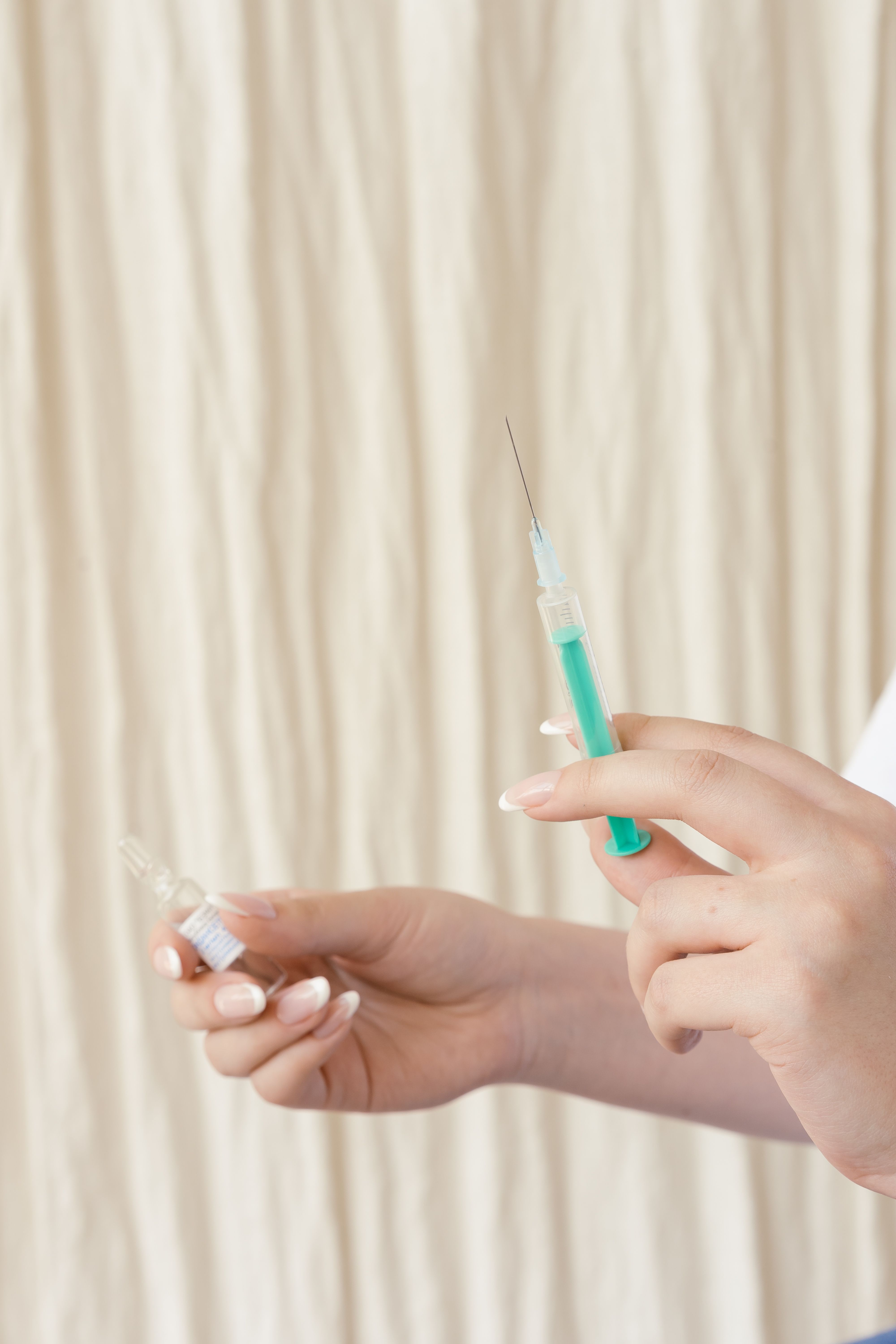 Hands holding a syringe and ampoule, preparing for medical injection in a healthcare setting.