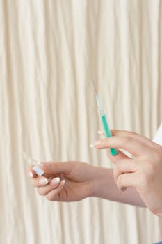 Hands holding a syringe and ampoule, preparing for medical injection in a healthcare setting.