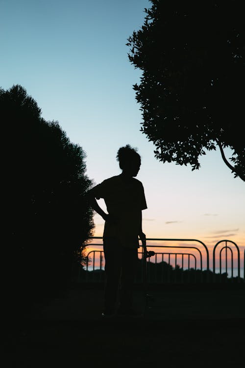 Silhouette of a Person Standing Near Fence during Sunset