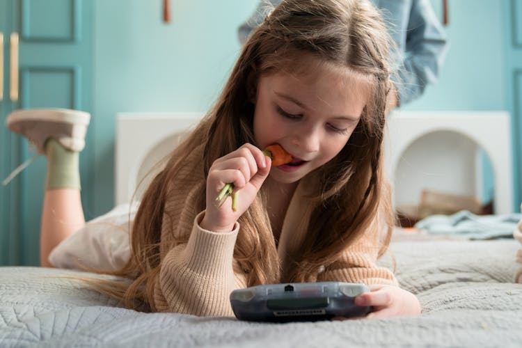 Young Girl  Eating Carrot While Playing A Video Game