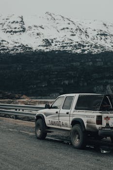 Toyota Hilux parked roadside with snowy mountains in background, showcasing rugged adventure.