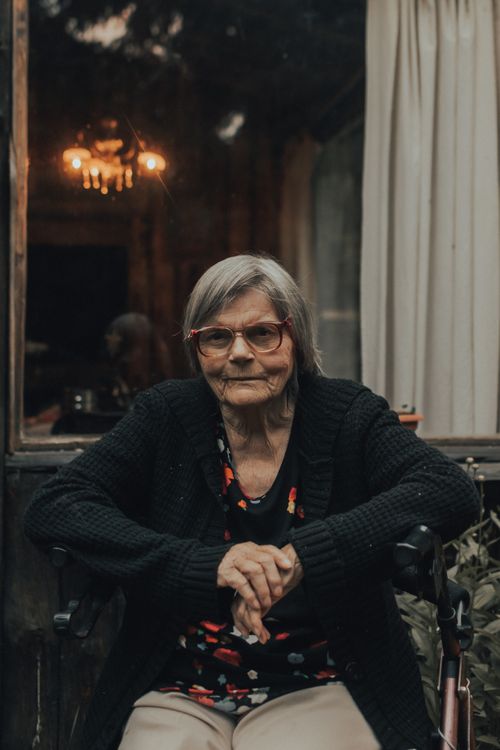 Free Senior woman with glasses sitting indoors at nighttime, wearing a black cardigan. Stock Photo