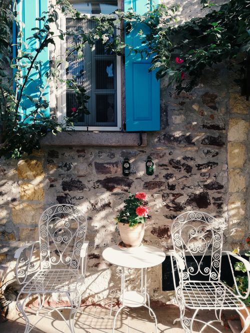 Free Picturesque patio with wrought iron chairs and a vibrant blue shuttered window. Stock Photo