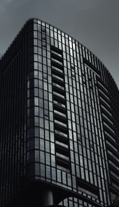 Free Low-angle shot of a modern skyscraper showcasing its sleek, glass facade in monochrome. Stock Photo