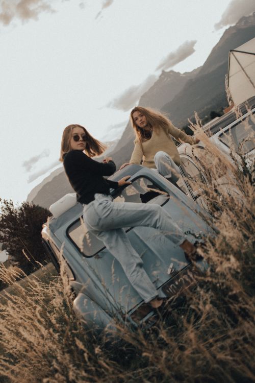Free Two women pose stylishly on a vintage car in a scenic outdoor setting. Stock Photo