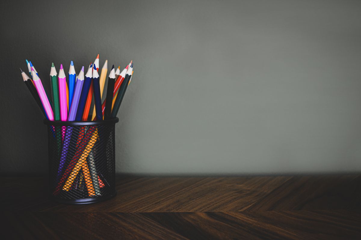 Colored pencils in a black mesh holder on a dark wooden desk