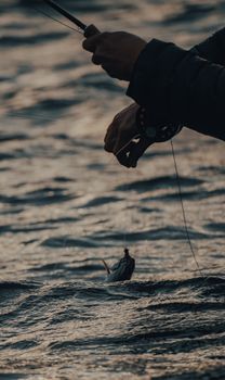 Close-up of hands fishing over calm waters at twilight, capturing a fish.