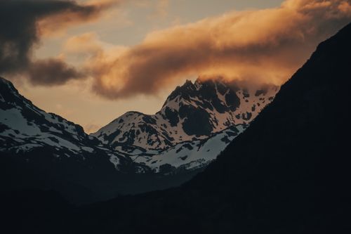 Free A breathtaking view of snowy mountains with dramatic clouds during sunset. Stock Photo