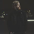 一个时尚的留胡子男人在夜晚的城市灯光下听着音乐