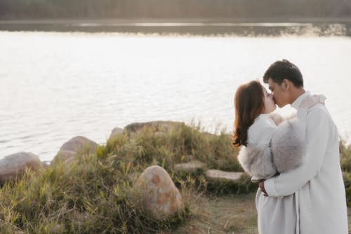 Couple Wearing Coats Kissing Beside a Lake