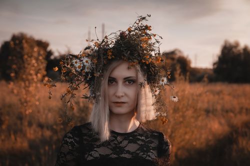 Free Portrait of a woman wearing a floral headdress in a serene field at sunset. Stock Photo