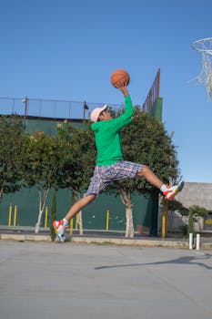 Athletic man jumping towards the hoop in an outdoor basketball court, showcasing skill and action.