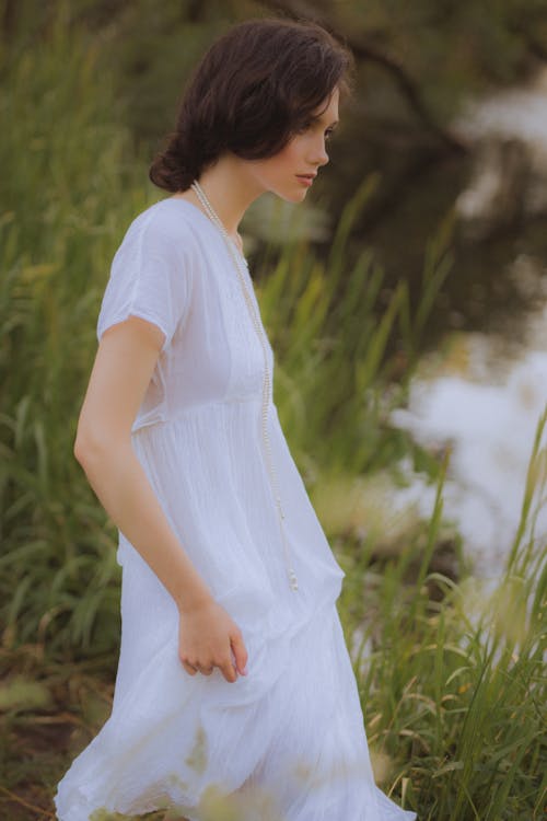 Side View of a Woman in White Dress in a Grass Field