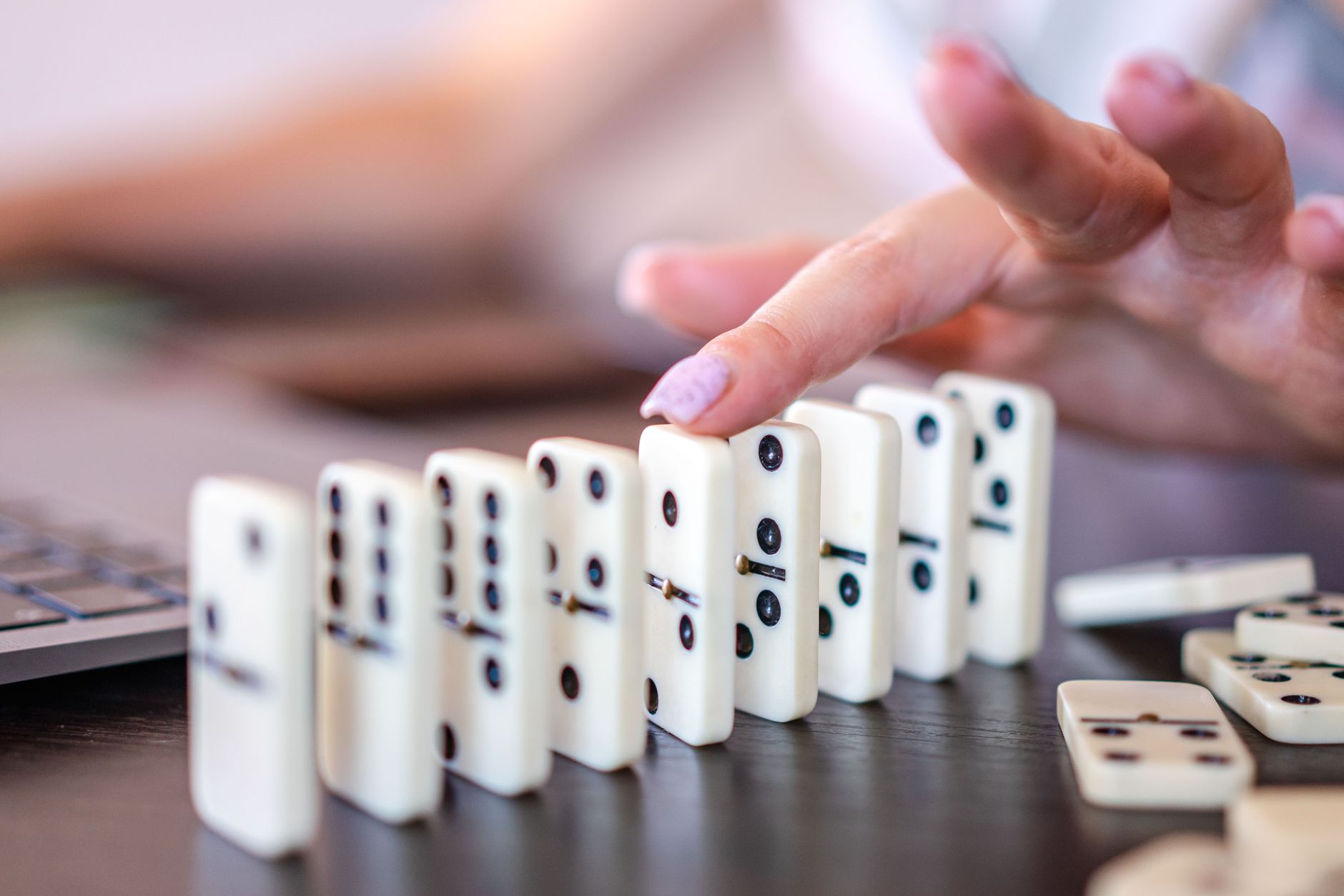 Fingers delicately push domino tiles, causing a chain reaction.