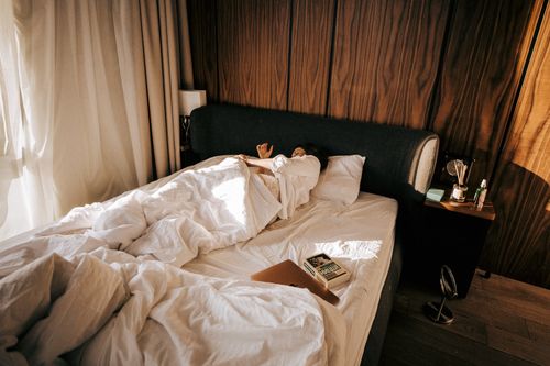 Free A comfortable hotel room featuring a woman sleeping under soft blankets, basking in morning sunlight. Stock Photo