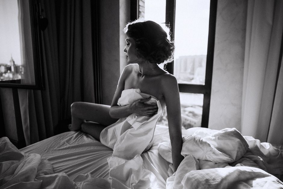Moody black and white photo of a woman in a bedroom setting, captured with dramatic lighting.