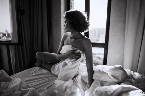 Free Moody black and white photo of a woman in a bedroom setting, captured with dramatic lighting. Stock Photo