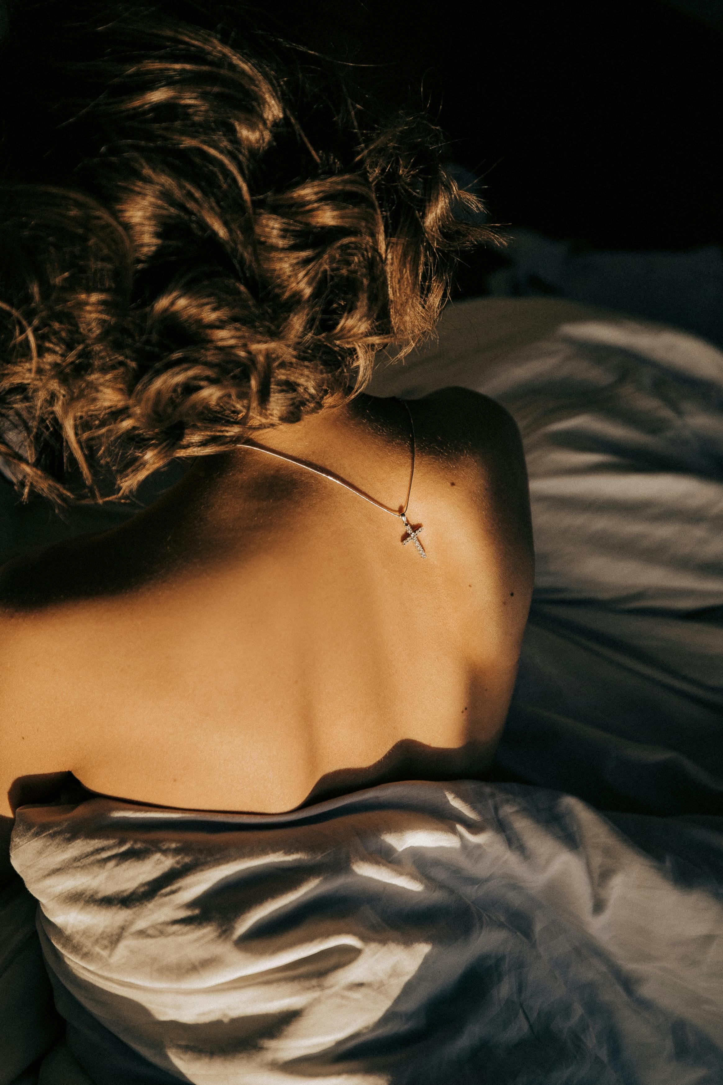 A woman peacefully lying in bed, bathed in warm morning light, showcasing tranquility.