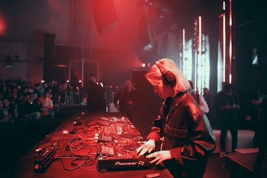 Female DJ in a leather jacket mixing music at a vibrant club party with red lighting.