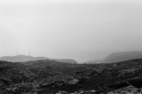 Grayscale Photo of a Piece of Land Near the Foggy Mountains 
