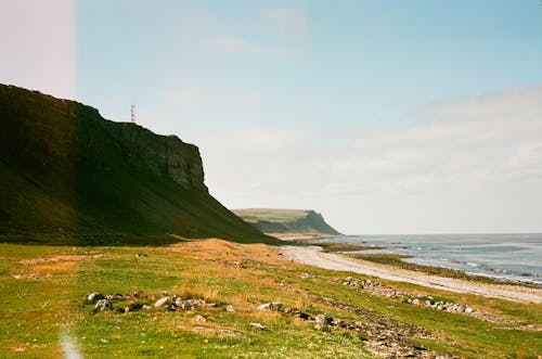 A Cliff Beside Green Grass Field Near the Shore