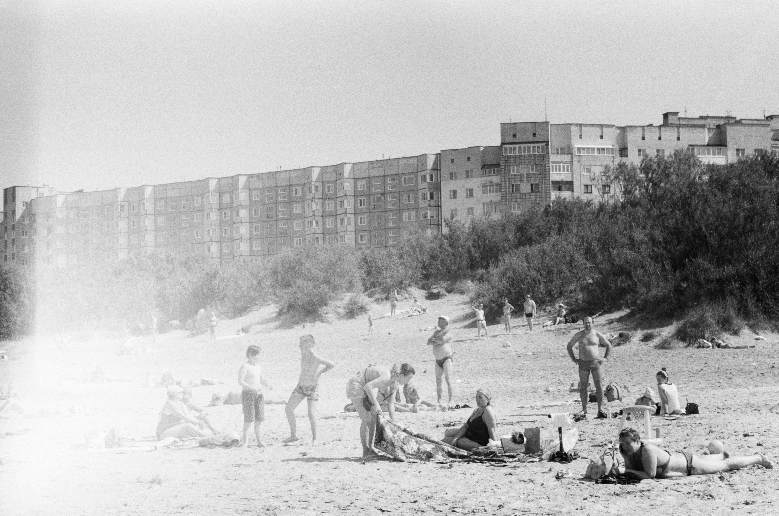 A vintage black and white photo of a bustling beach with urban apartments in the background.