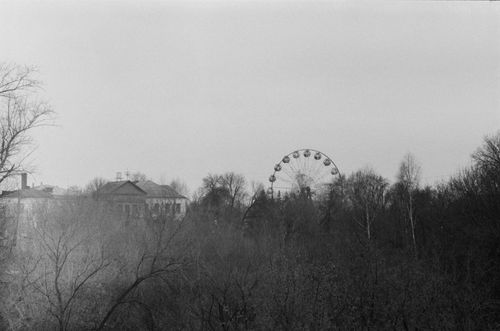 Free A black and white photo of a Ferris wheel viewed through mist and leafless trees. Stock Photo